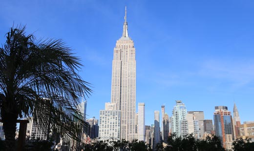 Vista frontal desde lejos del rascacielos Chrysler Building, rodeado de edificios mas pequeños y árboles.