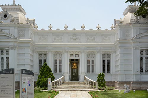 De frente se ve la entrada al museo, una construcción completamente blanca, con una grande puerta café  y grandes ventanas
