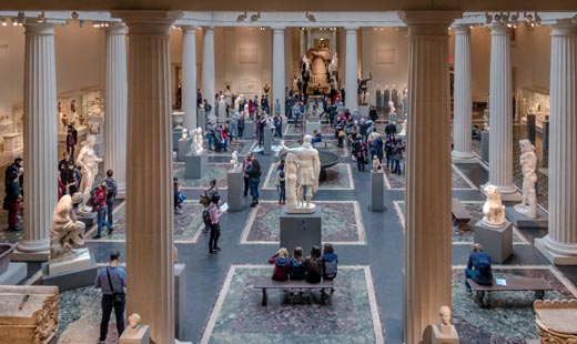 Una sala con grandes columnas, en las que se pueden ver varias esculturas y personas observándolas