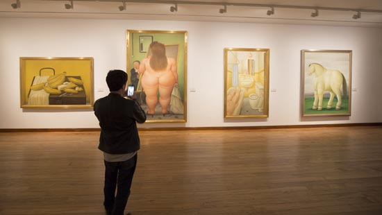 5.Interior de una galería de un museo, con 4 obras de Fernando Botero, en frente un joven tomandoles una foto.