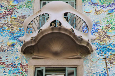 Imagen en ángulo contrapicado, de un balcón en forma de calavera, al lado las paredes del edificio llenas de piezas en cerámicas de diferentes colores