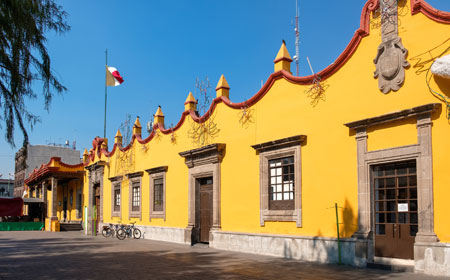 Fachada color ocre del ayuntamiento de coyoacán con la bandera de México