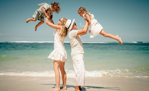 Una pareja de hombre y mujer en la playa y vestidos de blanco, alzan cada uno a un niño y una niña