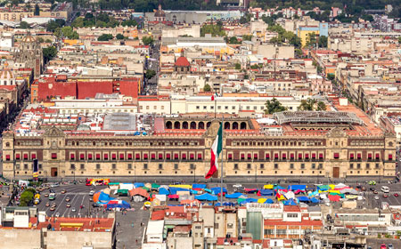 Panorámica aérea de la ciudad en la que se destaca el palacio de gobierno con la bandera de mexico y las construcciones adyacentes.