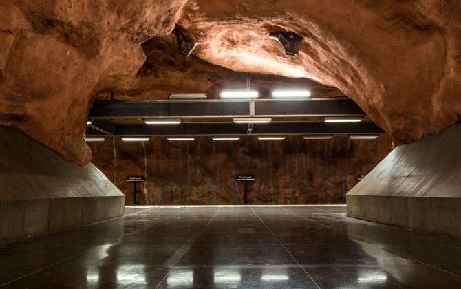 La estación de metro Rådhuset simula una cueva natural de arenisca, donde se destaca una columna gigante que desaparece en el techo en el que  hay dos botas ancladas, 