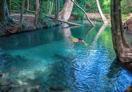Se ve una zona rodeada de árboles, con una laguna llena de las aguas cristalinas del río Cesar en donde se encuentra un hombre nadando