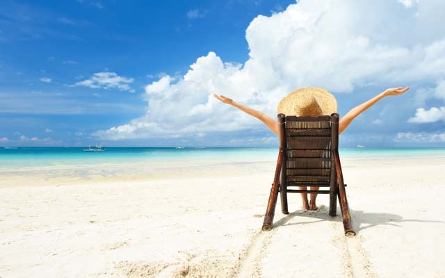 Una mujer con sombrero sentada en una silla rústica en la playa, frente al mar