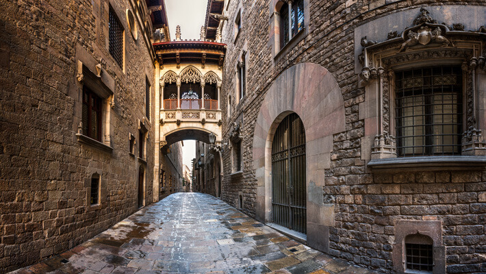 Calle estrecha con edificaciones altas con muchos detalles en sus fachadas y un puente que une dos construcciones de la calle