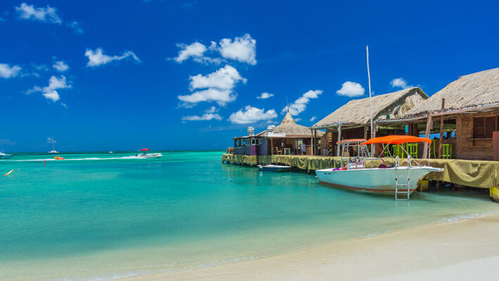Playa de Palm con agua azul y arena blanca, a un costado se observa el muelle con un bote
