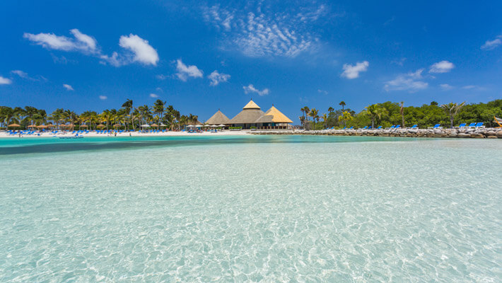 Playa Flamingo tiene agua color turquesa cristalina y arena blanca, de fondo se observa grandes palmeras con kioscos para los turistas